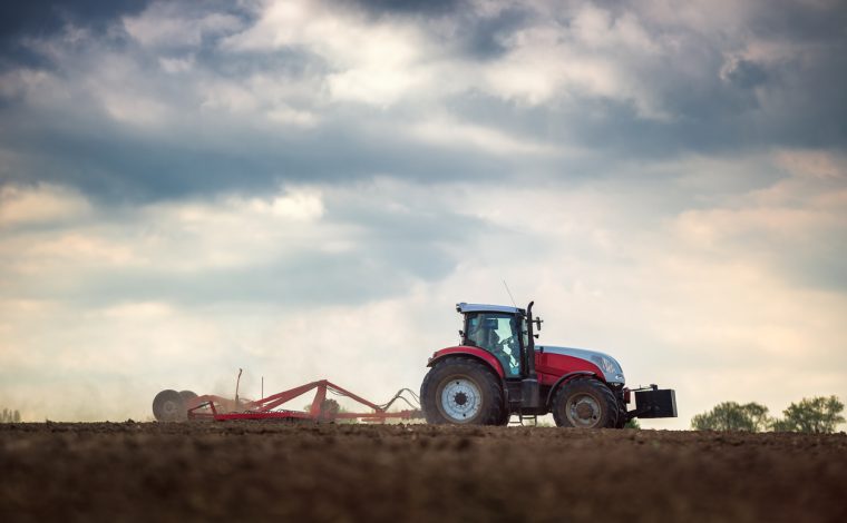 Farmer in tractor preparing land with seedbed cultivator, sunset shot